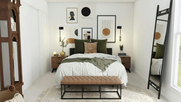 A modern eclectic bedroom featuring a bed with white linens and olive-green velvet pillows. A gallery wall of abstract art hangs above the headboard, flanked by two black wall-mounted sconces with long glass shades. To the left, a tall vintage grandfather clock stands in the corner, while a tufted cognac leather bench sits at the foot of the bed on a round Persian-style rug. A large black leaning floor mirror to the right reflects the bright, airy room.